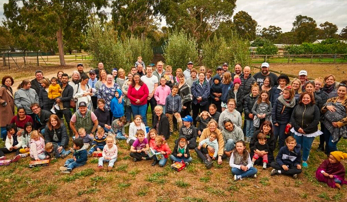 Members, Friends and Families of the Prader-Willi Syndrome Association of Victoria gathered together in a park, all smiling at the camera.